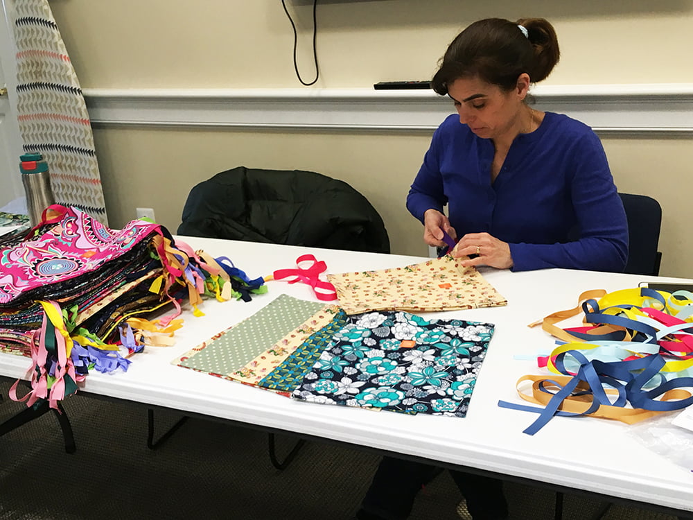 A parishioner works sits at a table cutting fabric to size for this sewing ministry. Multiple colors and patterns of fabric are laid out in front of her on the table.