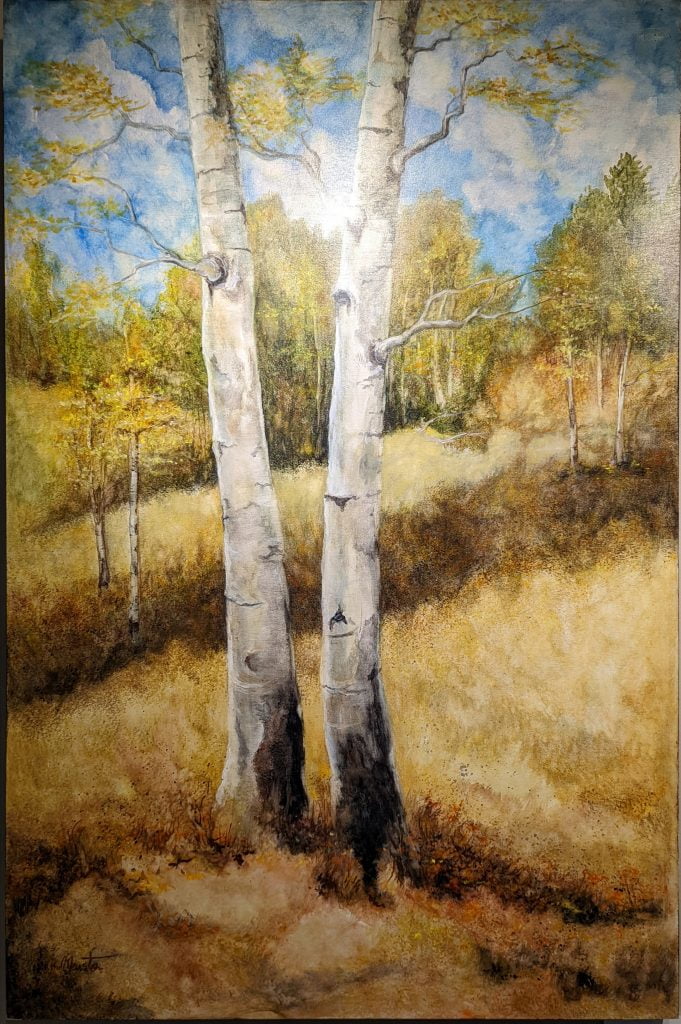 Stand By Me by Jeanne Marston is a watercolor on wood panel. Two narrow birch trees stand in a sparsely-treed field. They dominate the foreground and you cannot see their tops. They have grown very close together. The field is in yellow and brown tones, with the edge of the forest behind, and cloud speckled blue sky at top behind.